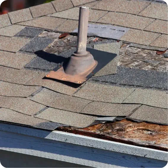 A closeup image of a severely damaged roof with rotting boards, missing shingles, and missing flashing around a pipe boot.