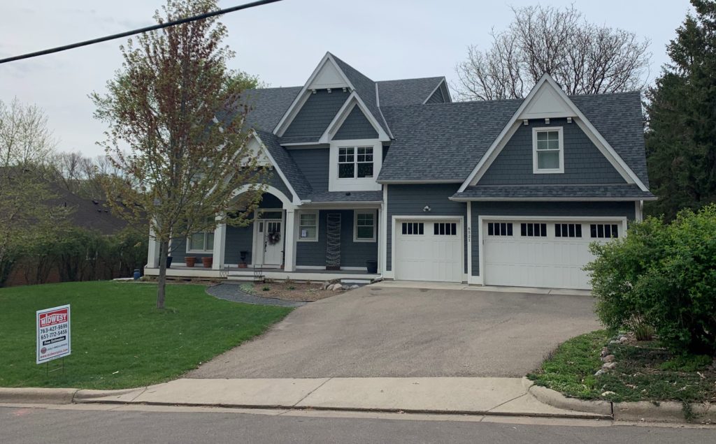 A two story home with gray siding and a new roof installed by Midwest Roofing Siding and Windows.