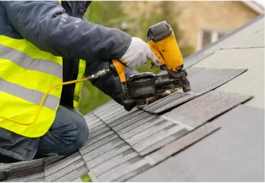 A team member with a nail gun installing shingles on a roof.